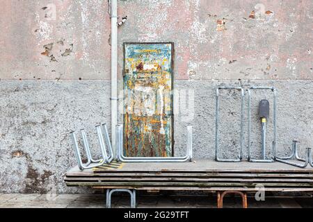 Several flood docks are stacked in front of a brick wall in pastel shades and a rusted, brightly painted metal door Stock Photo