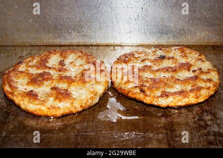 A pair of sausage patties cook on a flat grill in a restaurant. Stock Photo