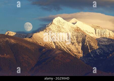 Moon rising over the snow-capped peaks of the Mission Mountain Range in western Montana - NOT photoshopped Stock Photo