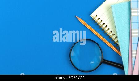 School flat lay composition with notebooks pencil and magnifying glass, student prepares for school days concept, blue background with copy space phot Stock Photo