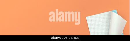 Banner with opened school checkered notebook on flat peach office table desktop background, copy space Stock Photo