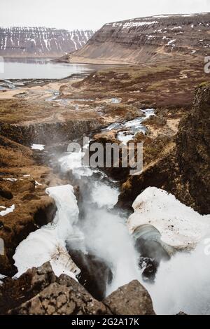 From above to misty flow of water falling from rocks in frost and running into lake among cliffs Stock Photo