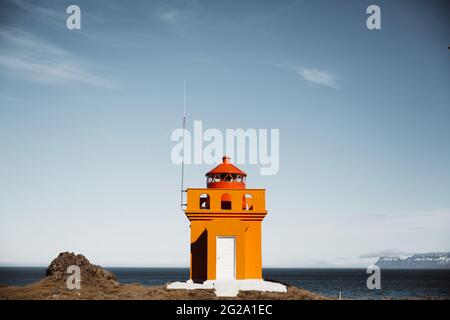 Wonderful view of small bright lighthouse standing on cliff near ocean on background of beautiful blue sky in Icelandic countryside Stock Photo