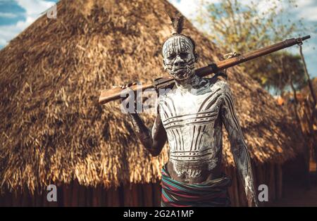 man with painted body holding a shotgun in Karo tribe village. Omo Valley, Ethiopia Stock Photo