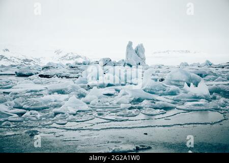 From above of white chunks of ice on calm lake water with remote snowy mountains and cloudy sky on background in Iceland Stock Photo