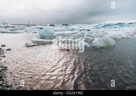 From above of white chunks of ice on calm lake water with remote snowy mountains and cloudy sky on background in Iceland Stock Photo