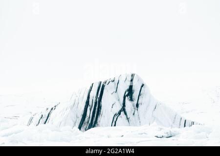 Block of white ice with blue stripes on remote snowy empty valley with white sky on background in Iceland Stock Photo