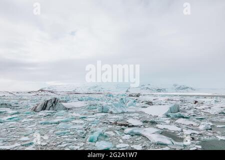 From above of white chunks of ice on calm lake water with remote snowy mountains and cloudy sky on background in Iceland Stock Photo