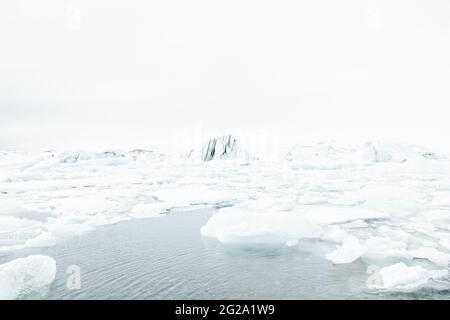 From above of white chunks of ice on calm lake water with remote snowy mountains and cloudy sky on background in Iceland Stock Photo