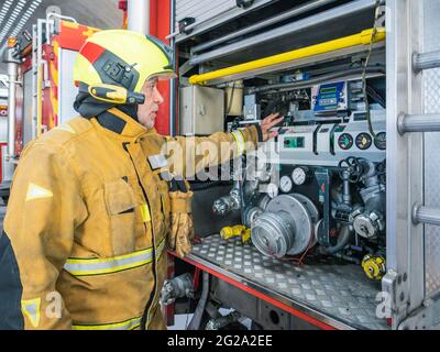 Equipped fireman standing and using an water engine into fire truck Stock Photo
