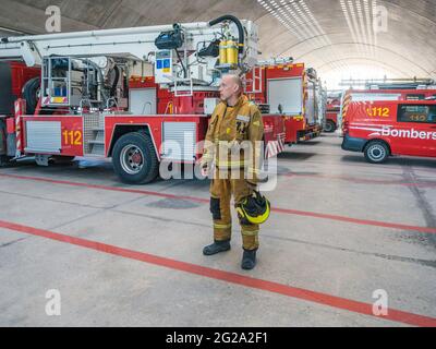 Professional fireman standing near fire truck and looking away Stock Photo
