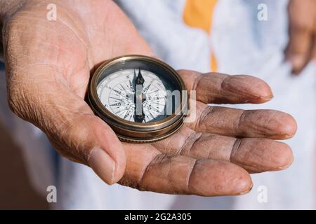 Unrecognizable ethnic traveler holding retro compass in wrinkled hands and standing on sand of Sahara Desert Stock Photo