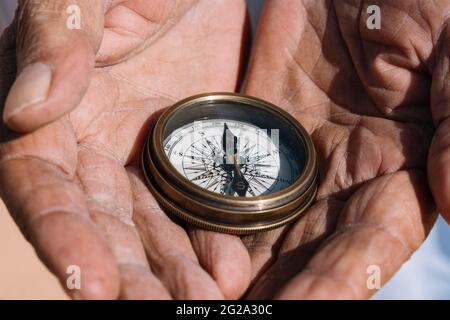 Unrecognizable ethnic traveler holding retro compass in wrinkled hands and standing on sand of Sahara Desert Stock Photo