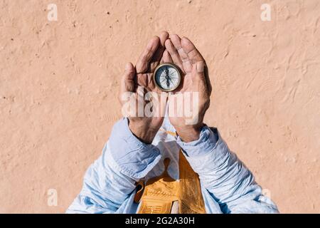 Unrecognizable ethnic traveler holding retro compass in wrinkled hands and standing on sand of Sahara Desert Stock Photo