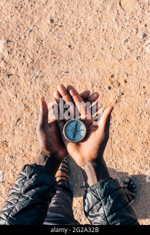 Unrecognizable African person holding retro compass in hands over dry sand of Sahara Desert Stock Photo