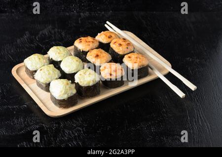 A set of seafood rice rolls wrapped with thin leaves of dried sea grass in a wooden platter on a black wooden background. Selective focus. Stock Photo