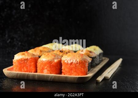 A set of various rolls with chopsticks in a wooden bamboo plate on a black wooden background. Selective focus. Stock Photo