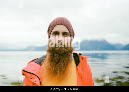 Bearded serious man in hat and coat standing near a lake looking at camera in Lapland Stock Photo