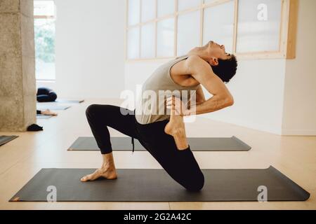 Side view of young slender man in sportive wear practicing yoga asana in training room in sunny day Stock Photo
