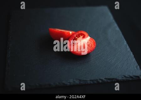 group of tomatoes, one cut in half, rests on a black board for serving Stock Photo