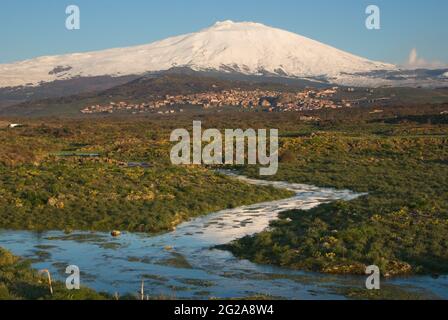 a seasonal river flows under the massive snowcovered Etna volcano at the evening Stock Photo