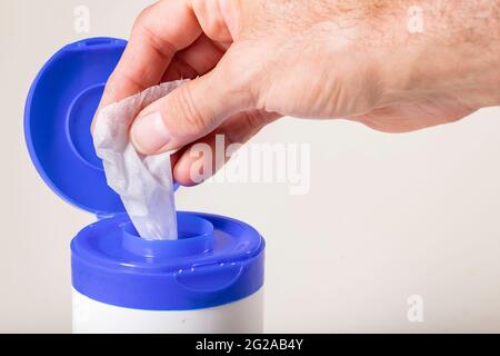White wipes soaked in disinfectant pulled out by a male's hand. Household surface decontamination accessories. Isolated background. Stock Photo