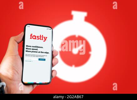 San Francisco, CA, USA, June 2021: A hand holding a phone with the Fastly app on the screen. Red background with blurred Fastly logo. Fastly is an Ame Stock Photo