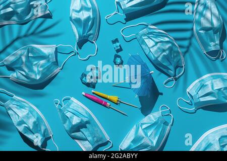 pattern with many medical masks, ice cubes and beach umbrellas isolated on a bright blue background. hard shadows from the sun at noon Stock Photo