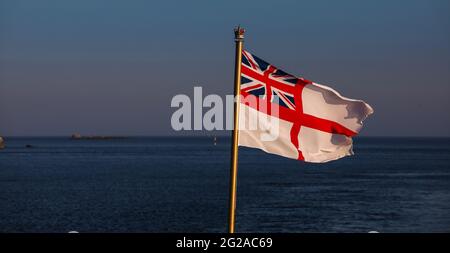 The flag of the British Royal Navy the White Ensign being flown from the ensign staff of a British warship Stock Photo