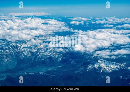 Travel concept. A beautiful view from an airplane on white voluminous fluffy clouds over snow-capped mountains and blue sky. Top view. Stock Photo