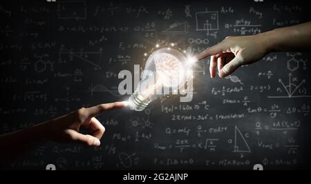 Hand pointing a brain inside a light bulb on wall backboard or chalkboard background. Business bright idea, Great idea for success, and Mixed media. Stock Photo