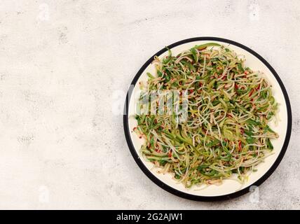 Mung bean sprouts salad with cucumbers and radishes in a white plate on a light background. Top view, flat lay Stock Photo