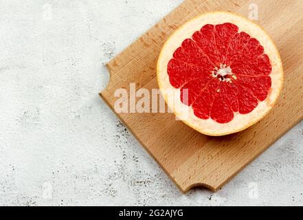 Sliced red grapefruit on a wooden cutting board on a light gray background. Top view, flat lay Stock Photo