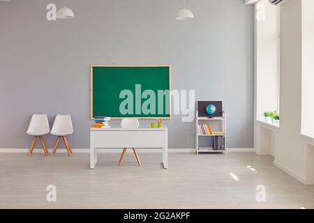 Interior of empty school classroom with teacher's desk and clean green blackboard Stock Photo