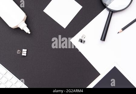 Workplace mockup in contrast black and white tones. Office desk with stationery, book, blank sheet, magnifier, keyboard and pencil. Top view, space fo Stock Photo