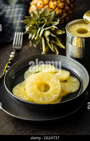 Canned sliced pineapple fruit on plate on black table. Stock Photo
