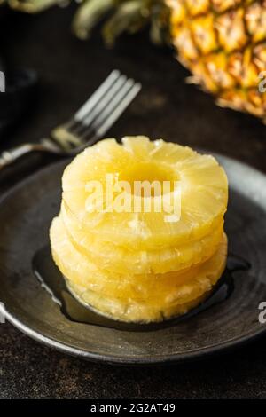 Canned sliced pineapple fruit on plate on black table. Stock Photo