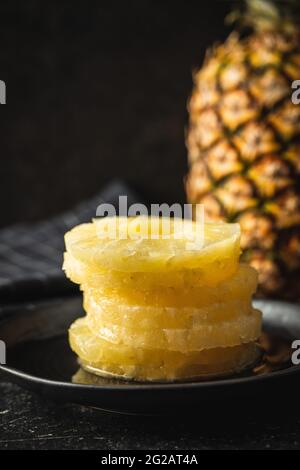 Canned sliced pineapple fruit on plate on black table. Stock Photo