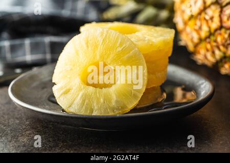 Canned sliced pineapple fruit on plate on black table. Stock Photo