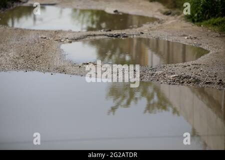 Shallow depth of field (selective focus) details with huge potholes filled with water after a rain in a mud road in Bucharest, Romania. Stock Photo