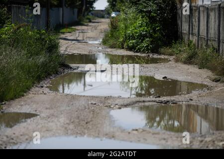 Shallow depth of field (selective focus) details with huge potholes filled with water after a rain in a mud road in Bucharest, Romania. Stock Photo