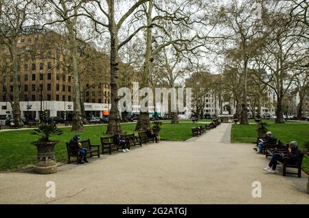 London, UK - April 21, 2021: People enjoying the public benches in the famous Berkeley Square in Mayfair, London on a chilly spring afternoon. Stock Photo