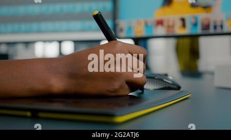 Close up of photo designer editing with tablet and pencil, illustrator drawing on graphics tablet. Hand of african woman retoucher using stylus pen retouching assets sitting in creative agency office Stock Photo