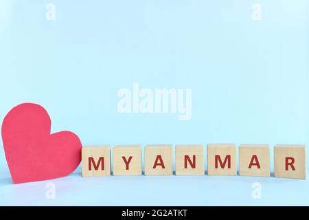 Myanmar word on wooden blocks with red heart shape cutout in blue background. Support, sympathy pray, and send love to Myanmar concept. Stock Photo