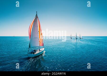 Regatta sailing ship yachts with white sails at opened sea. Aerial view of sailboat in windy condition. Stock Photo