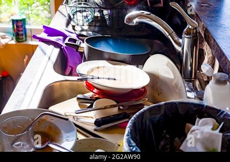 A big pile of dirty dishes, pots, utensils stacked into kitchen sink. Concept image for hand washing dishes, mess in kitchen, chores, eyesore. Common Stock Photo
