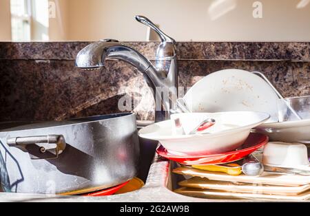 Close up frontal view of a kitchen mess with dirty pots, dishes and utensils have piled up in kitchen sink in front of the faucet. They are waiting to Stock Photo