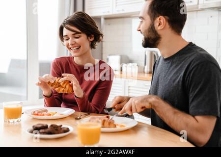 Cheerful attractive young couple having tasty breakfast at the kitchen table Stock Photo