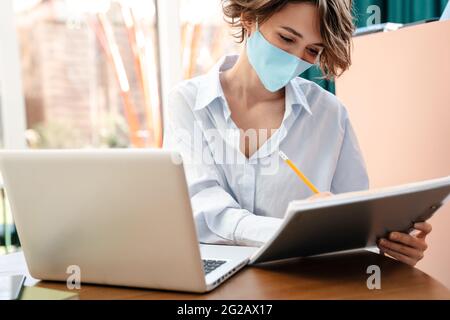 Attractive young businesswoman working from a cafe inddoors, taking notes Stock Photo