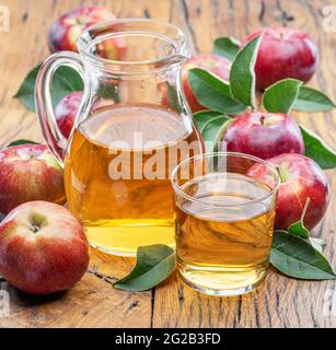 Glass and carafe of fresh apple juice and organic apples on dark old wooden table. Stock Photo